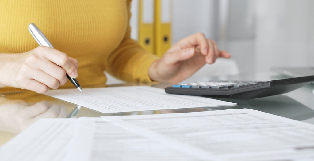 Gros plan sur des mains tapant sur un clavier d'ordinateur moderne, feuille de calcul financier floutée en arrière-plan, bureau épuré